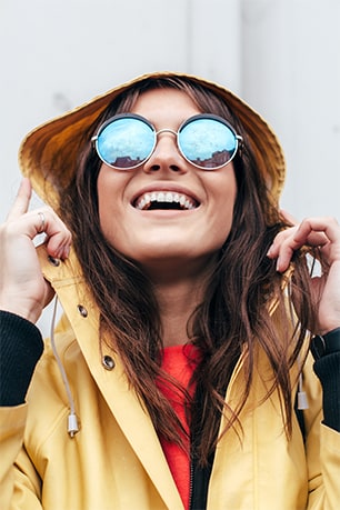 Happy and smiling Tripolis-Park occupant wearing a yellow raincoat and reflective sunglasses looking upwards.
